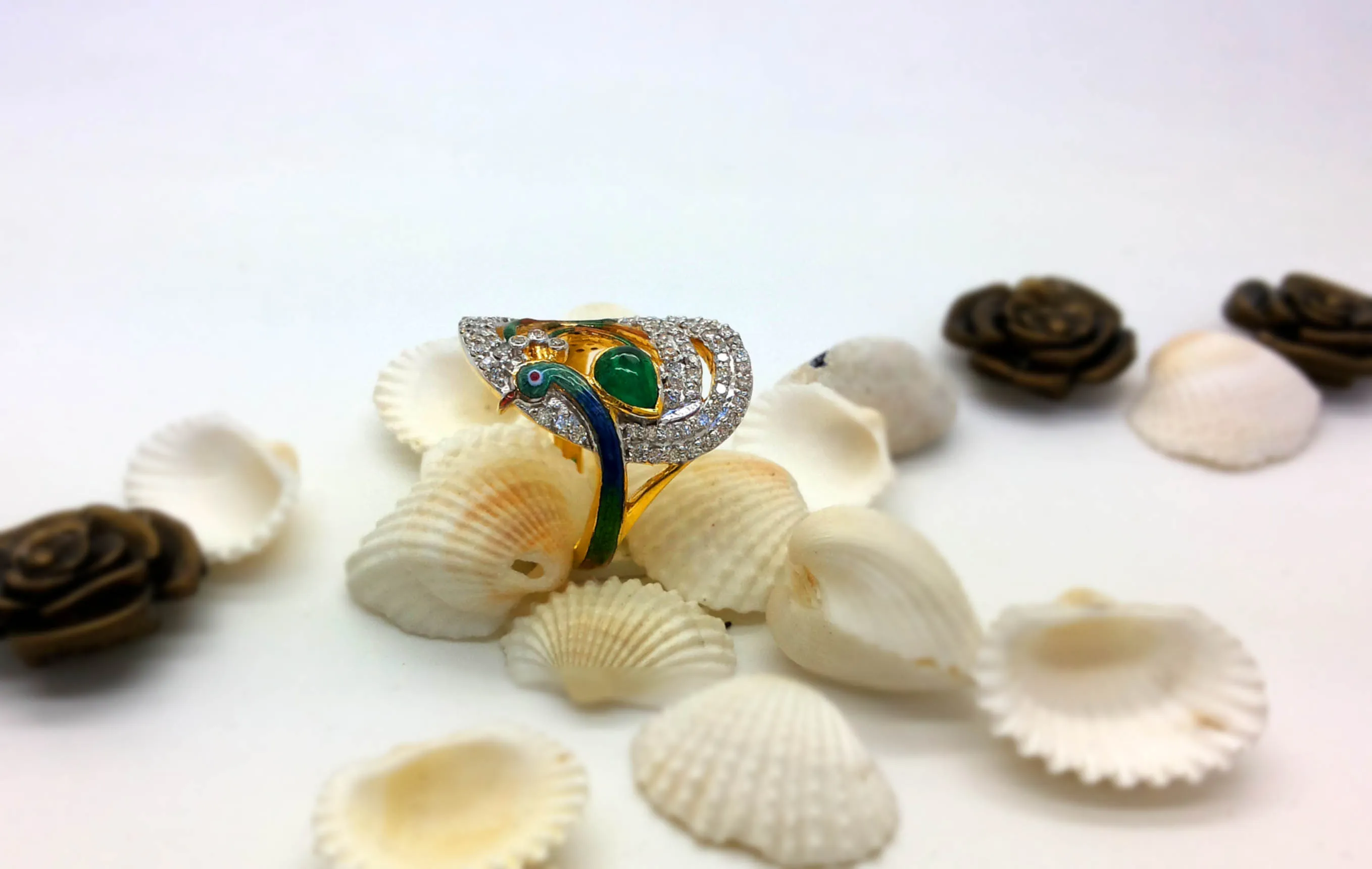 Diamond pavé ring with a deep green centre stone, photographed among small shells